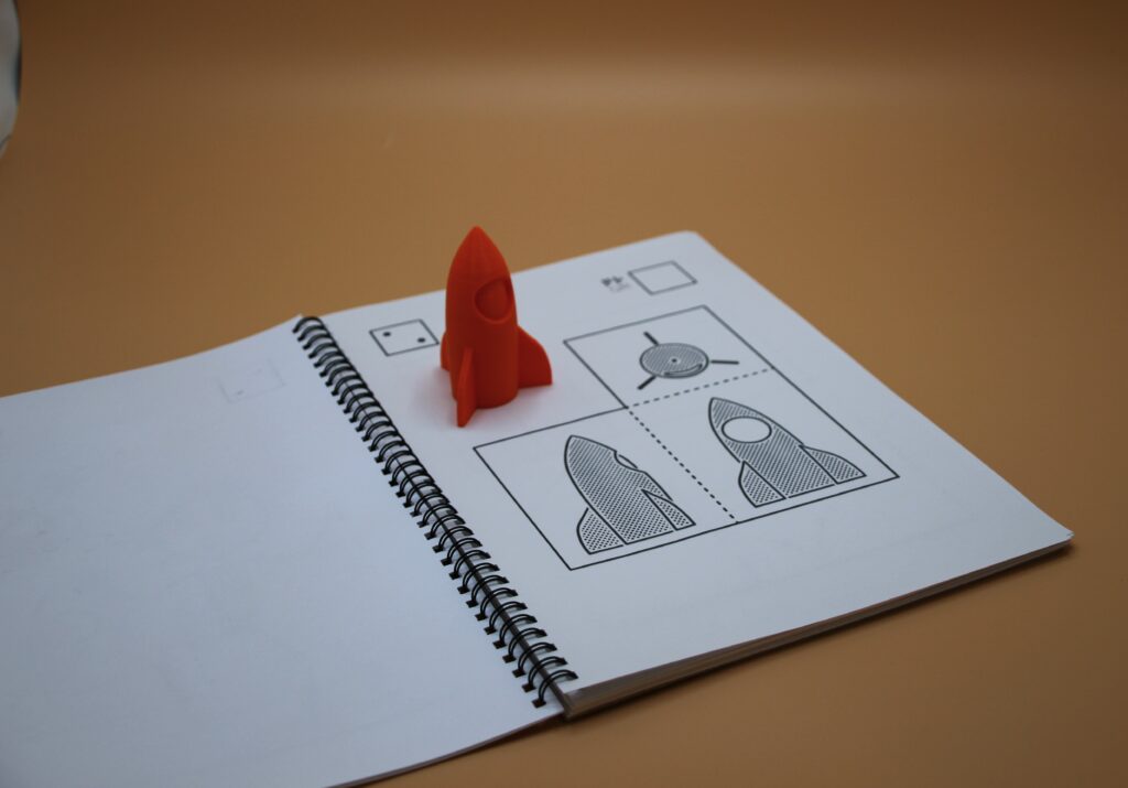 The second page of the book Roundy, showing a rocket from three angles. A 3D model of the rocket has been placed on the book.